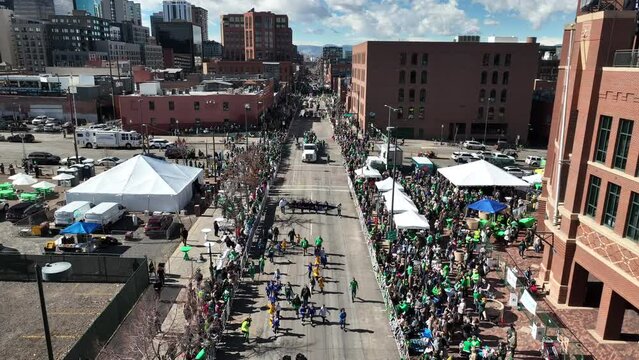 Overhead aerial view of a Saint Patrick's Day parade as people in green clothing march through the streets.