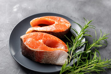 Steak of fresh raw red fish salmon with lemon, rosemary and pepper on black background