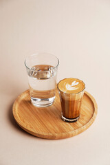 Coffee art latte and glass of water on wooden tray