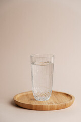 Glass of water on wooden tray, light background