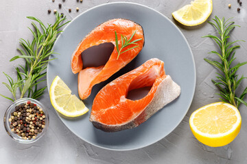 Steak of fresh raw red fish salmon with lemon, rosemary and pepper on grey background
