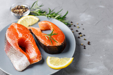 Steak of fresh raw red fish salmon with lemon, rosemary and pepper on grey background