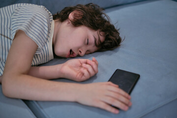 A 7-year-old boy sleeps on the couch at home with a phone in his hands, highlighting concerns about children's sleep and how mobile devices can impact their well-being.