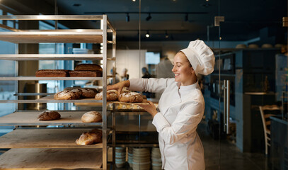 Beautiful woman baker in uniform checking freshly baked bread