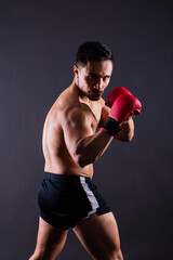 Plakat Muscular model sports young man in boxing gloves on grey background. Male flexing his muscles.