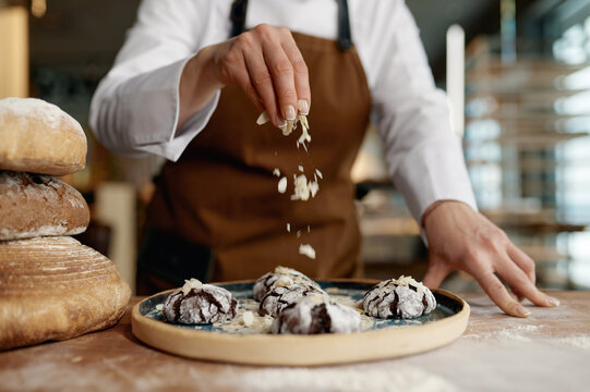 Baker chef sprinkling freshly baked oatmeal cookies with cereals