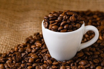 Full cup of roasted coffee beans in table covered by sackcloth, natural warm colors, morning drink beverage