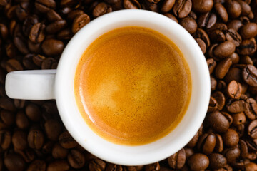 Top view of brewed espresso in cup at whole roasted coffee beans background, morning invigorating drink