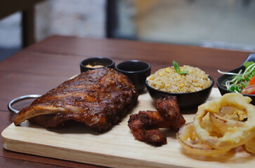 Grilled pork bbq ribs served with cherry tomatoes. basil and barbeque sauce on wooden cutting board over dark background. Close up