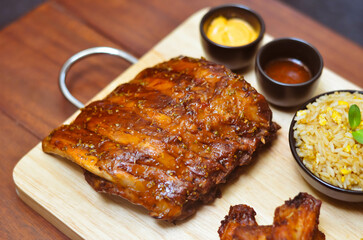 Grilled pork bbq ribs served with cherry tomatoes. basil and barbeque sauce on wooden cutting board over dark background. Close up