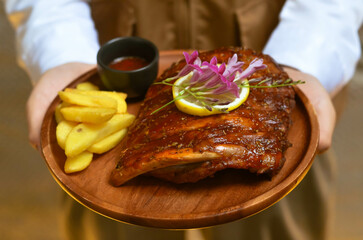 Grilled pork bbq ribs served with cherry tomatoes. basil and barbeque sauce on wooden cutting board over dark background. Close up