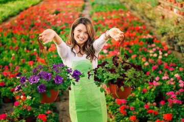Fototapeta premium Happy nursery garden worker holding pots with flowers and relocating it.
