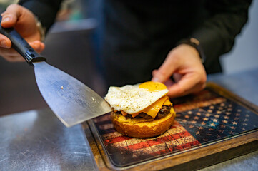 chef hand cooking cheeseburger with vegetables and egg on restaurant kitchen