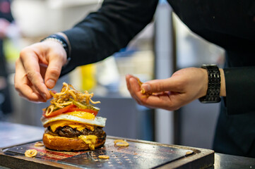 chef hand cooking cheeseburger with vegetables and egg on restaurant kitchen