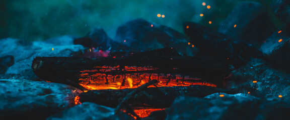 Fototapeta na wymiar Vivid smoldered firewoods burned in fire close-up. Atmospheric warm background with orange flame of campfire and blue smoke. Wonderful full frame image of bonfire. Burning logs in beautiful fire.
