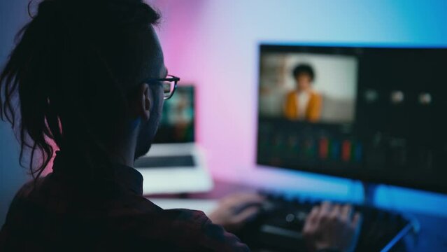 Young man in glasses working on video editing on computer doing montage and color correction. Professional man hand making edits on a special panel. Concept of creating video content.