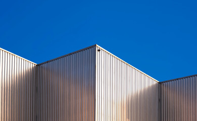 Fototapeta na wymiar Corrugated Steel Wall of Industrial Factory Buildings against blue clear sky background with light reflection on surface