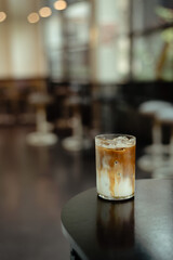 A glass of iced coffee sits on a table in front of a bar.