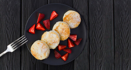 Cheese pancakes and strawberry on the dark plate on the black wooden background.Top view.Copy space.Cheese pancakes and strawberry on the dark plate on the black wooden background.Top view.Copy space.