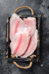 Fresh tilapia white fish fillet in a wooden tray. Black background. Top view
