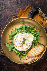 Salad with grilled Camembert cheese, arugula, toast and rosemary in a plate. Dark background. Top...