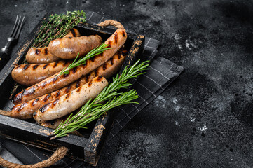 Fried on a grill skillet mix sausages in a wooden tray with herbs. Black background. Top view. Copy...