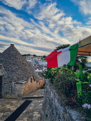 Fototapeta na wymiar Sunset with Trulli houses and the Italian flag in Alberobello, Puglia, Italy, Italia