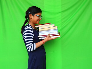 Girl with glasses holding books in his hands and looking at books , side view, green background 