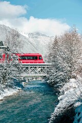 Red Train Crossing Bridge over Blue Water River With Snowy Mountains and Trees  in French Alps 