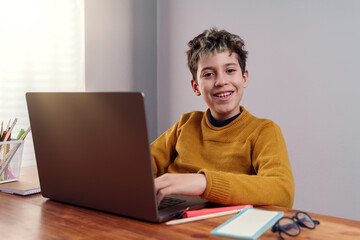 Smiling ten-year-old boy doing homework on laptop at desk
