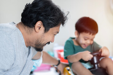 Asian dad sitting on floor playing with toddler son with toy cars at home