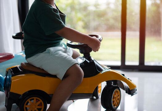 Cropped image of little Asian boy driving children's electric toy car near the door at home.