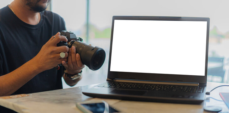 Handsome young photographer using a camera while working with a laptop with blank screen