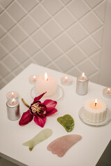 Obraz na płótnie Canvas Gua sha tool. Candles, and orchid flowers on table. Facial massage for lifting, face therapy, home spa, mockup. Skincare concept. Cosmetology, body massage, spa procedure. Details decor in spa salon.