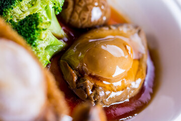 expensive premium braised head abalone with sea cucumber and flower mushroom broccoli in thick golden sauce on wood table asian chinese halal deluxe banquet seafood menu 