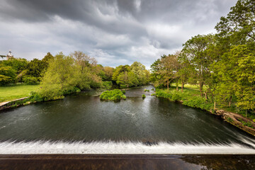 View from the Mortain (blue) bridge over the weir on the River Stour in Blandford Forum. In the distance is the Georgian bell tower of the parish church of St Peter and St Paul.