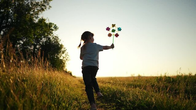 kid girl run after a pinwheel toy in a beautiful city park. kid girl fun run and playing in the park. Adventures in the park: the girl play, run and has fun with a toy lifestyle pinwheel