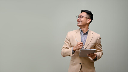 Smiling Asian businessman looking aside at the empty space, holding a tablet