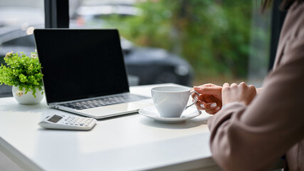 Close-up image of a businesswoman sipping coffee at her desk in the office.