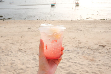 Hand holding strawberry lemon soda in take away cup (plastic glass) on the beach background.