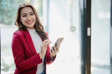 Fototapeta premium Portrait of beautiful young businesswoman standing smiling and using smartphone