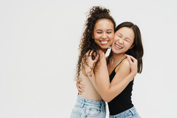 Fototapeta premium Two cheery girls hugging while standing with eyes closed isolated over white background