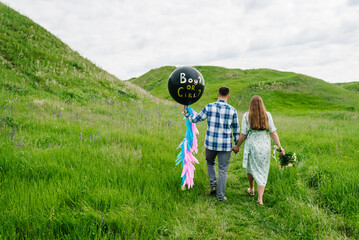 Baby shower party in a field or meadow. Man and woman holding a black balloon with 