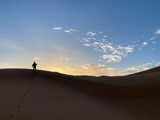 Fototapeta na wymiar A silhouette of a man climbing a sand dune towards the sunrise Morocco 