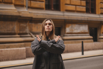 Woman arms crossed at her chest demonstrates Break The Bias symbol of international women's day principles of feminism, gender equality and support. Woman show stop sign on the street in city.