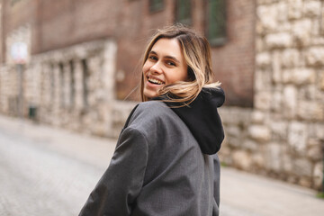 Fototapeta premium Young beautiful smiling hipster woman in trendy outfit. Sexy carefree woman posing on the street. Cheerful and happy girl wear grey suit and black hoodie turn around. Lifestyle, female beauty concept.