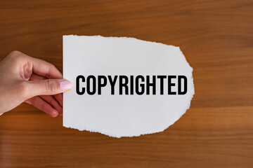 Copyrighted. Woman hand holds a piece of paper with the note copyright. Intellectual property, legal right, protection, judicial system, private property, patent and forbidden. 