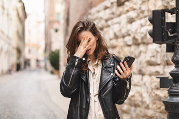 Sad woman checking bad news on mobile phone complaining alone in the street. Upset young woman...