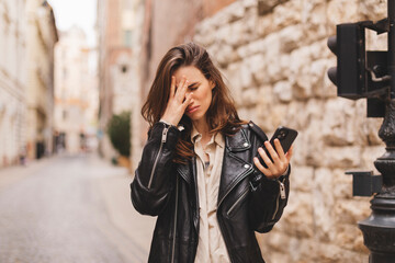 Sad woman checking bad news on mobile phone complaining alone in the street. Upset young woman...