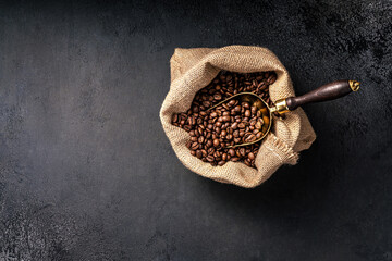Scoop of coffee beans in a bag on dark background. Top view of coffee. Copy space for text.